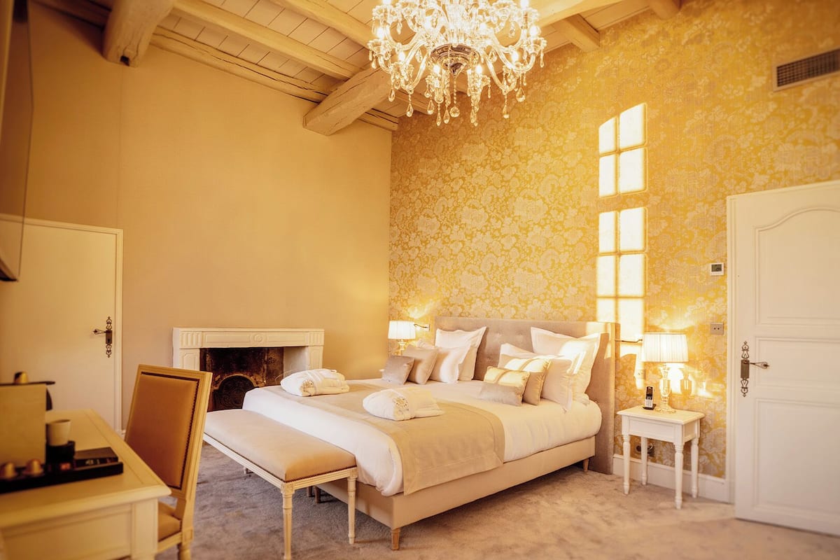 A bedroom with a large bed, a chandelier, a fireplace, and a door.