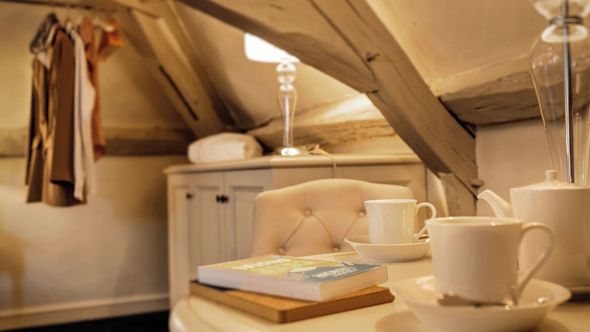 Una habitación acogedora con una mesa preparada para tomar té, un libro y una lámpara.