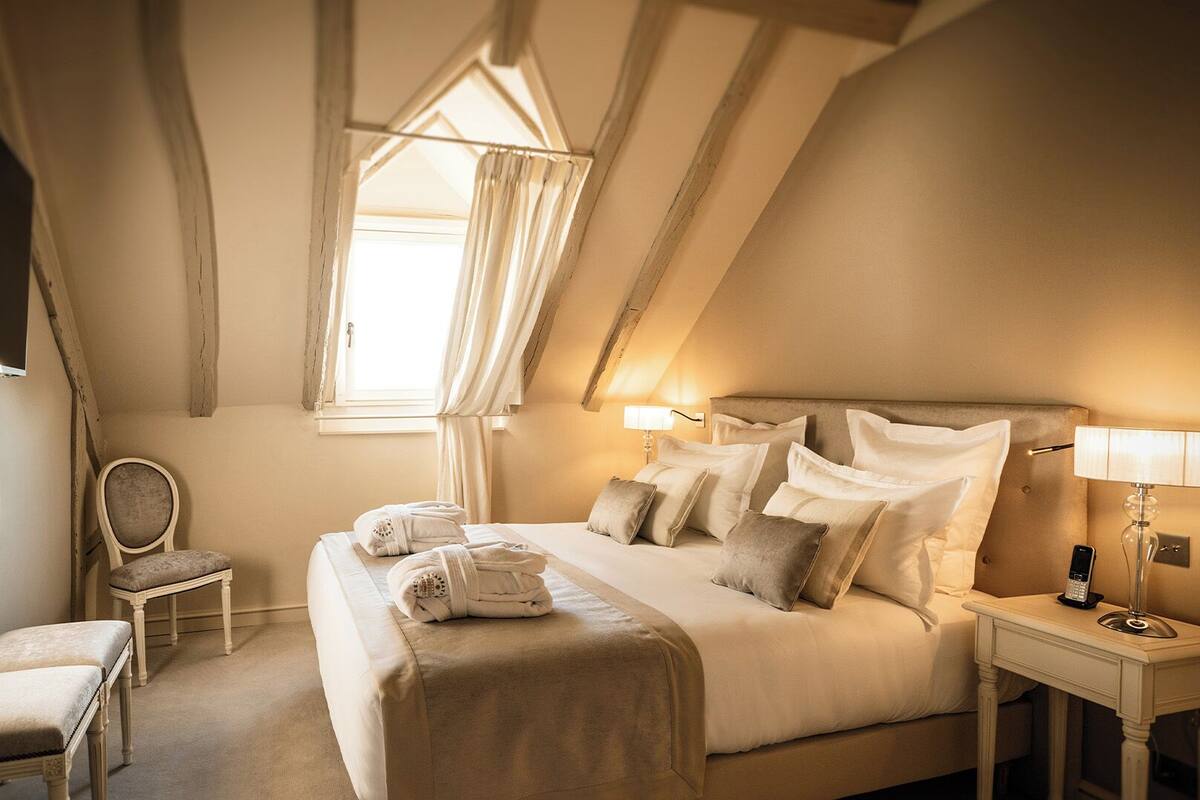 A hotel room with a large bed, two bedside lamps, a chair, and a TV mounted on the wall.