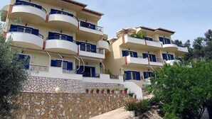 A multi-story residential building with balconies, a stone wall, and potted plants. - La Casa Di Nonna Anna (Lefkada)