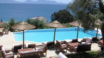 A pool with lounge chairs and umbrellas, overlooking a body of water and distant mountains.