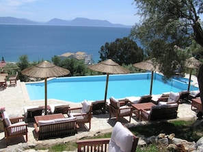 A pool with lounge chairs and umbrellas, overlooking a body of water and distant mountains. - La Casa Di Nonna Anna (Lefkada)