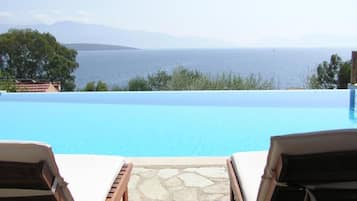 A pool with a view of the sea, two lounge chairs, and a stone-tiled deck.