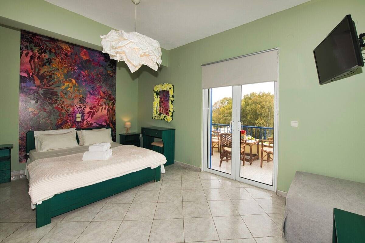 Un dormitorio con una cama grande, un cuadro abstracto y colorido, una puerta corrediza al balcón y un televisor de pantalla plana montado en la pared.