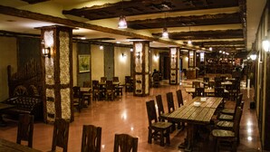 A spacious restaurant with wooden tables and chairs, stone pillars, and hanging pendant lights. - Dubai International Hotel (Baku)