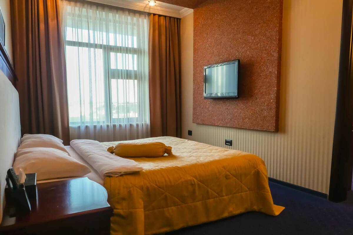Une chambre d’hôtel avec un lit, un téléviseur fixé au mur et une fenêtre avec des rideaux.