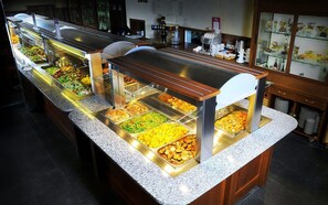 A buffet setup with various food items in glass containers, a coffee station, and a display case with pastries.