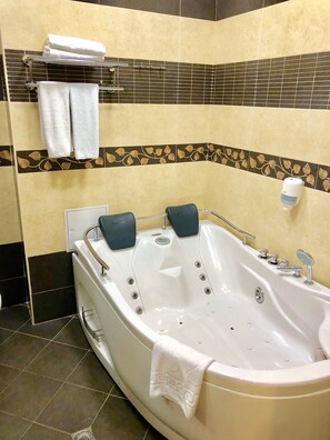 A bathroom with a large bathtub, two towels on a rack, and a soap dispenser.