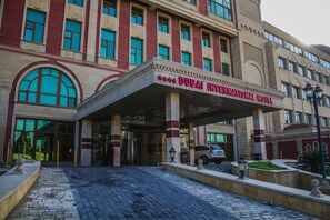 The exterior of the Dubai International Hotel with a grand entrance, large windows, and a red and beige facade.