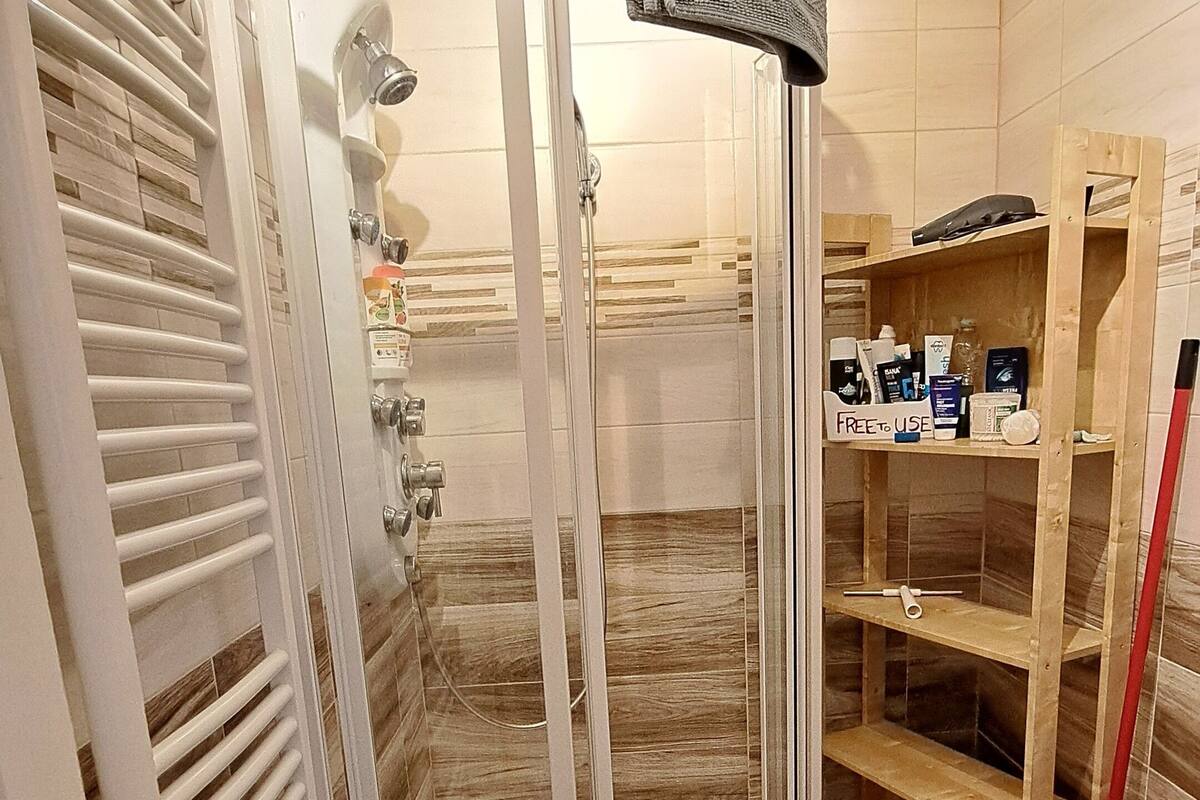 A shower area with a glass door, a towel rack, and a shelf with toiletries.