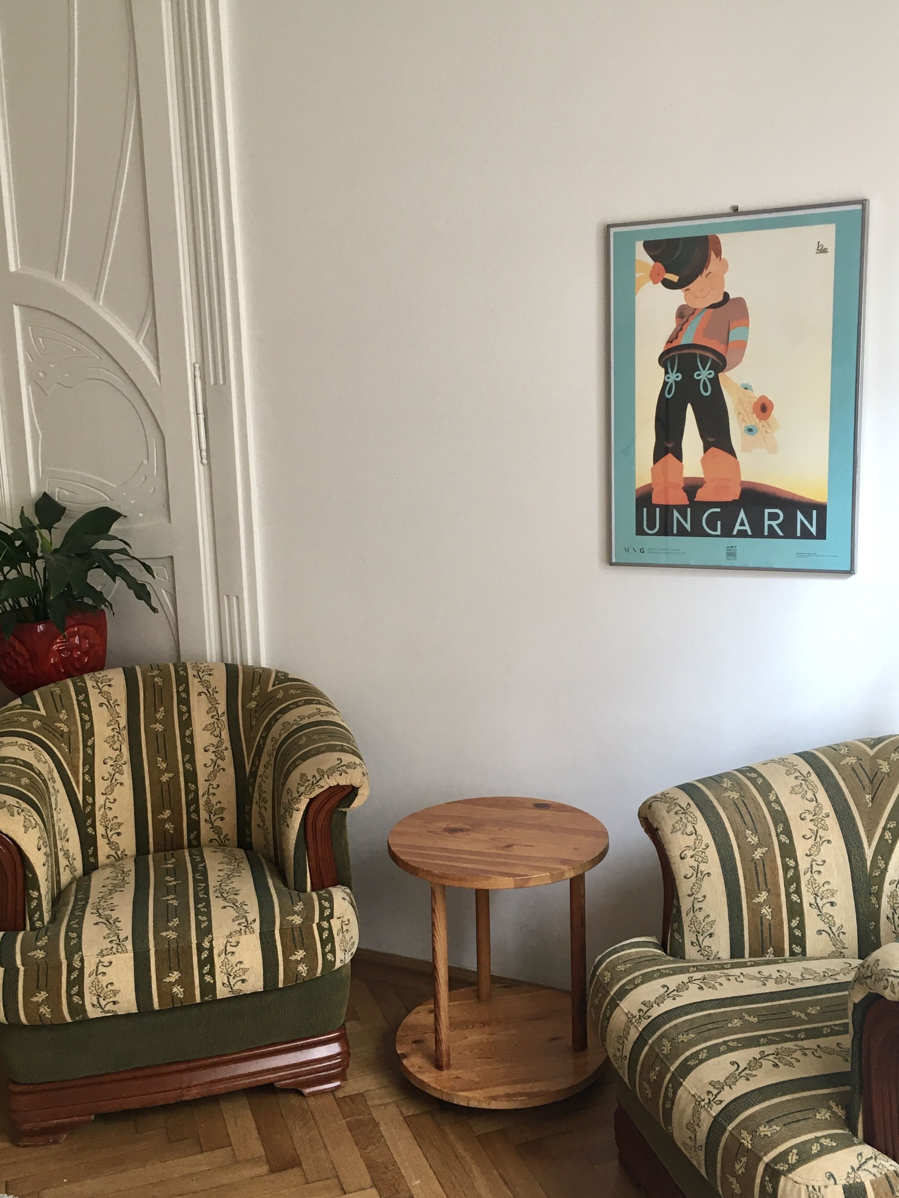 Une pièce comprenant deux fauteuils à motifs, une petite table en bois et une affiche accrochée au mur.