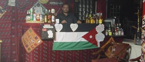 A bar area with a flag, shelves of bottles, and a wooden chair.