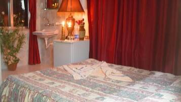 A bedroom with a bed, a bedside table, a lamp, a sink, and a window with curtains.