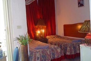 A room with two beds, a red curtain, a lamp, and a small plant. - Valentine Inn (Wadi Musa)