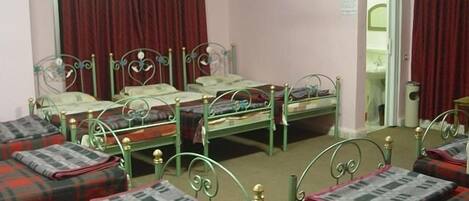 A room with four single beds, each with a plaid blanket and green metal headboards.