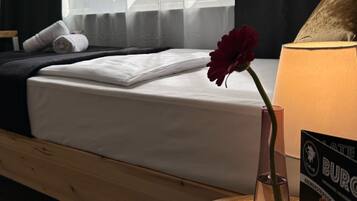 A hotel room with a bed, a vase with a flower, a table with a lamp, and a poster on the wall.