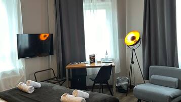A hotel room with a bed, a desk, a chair, a TV, and a floor lamp.