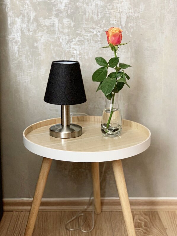 A round wooden table with a black lamp and a glass vase containing a single rose.