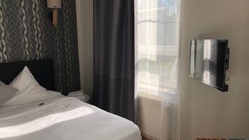 Ein Hotelzimmer mit einem Bett, einem an der Wand montierten Fernseher, einem Fenster mit durchsichtigen Vorhängen und einem strukturierten Wandpapier.