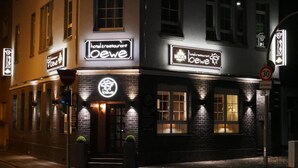 Un hotel y restaurante llamado 'oewe' con letreros iluminados, fachada de ladrillo y una señal de límite de velocidad de 30.