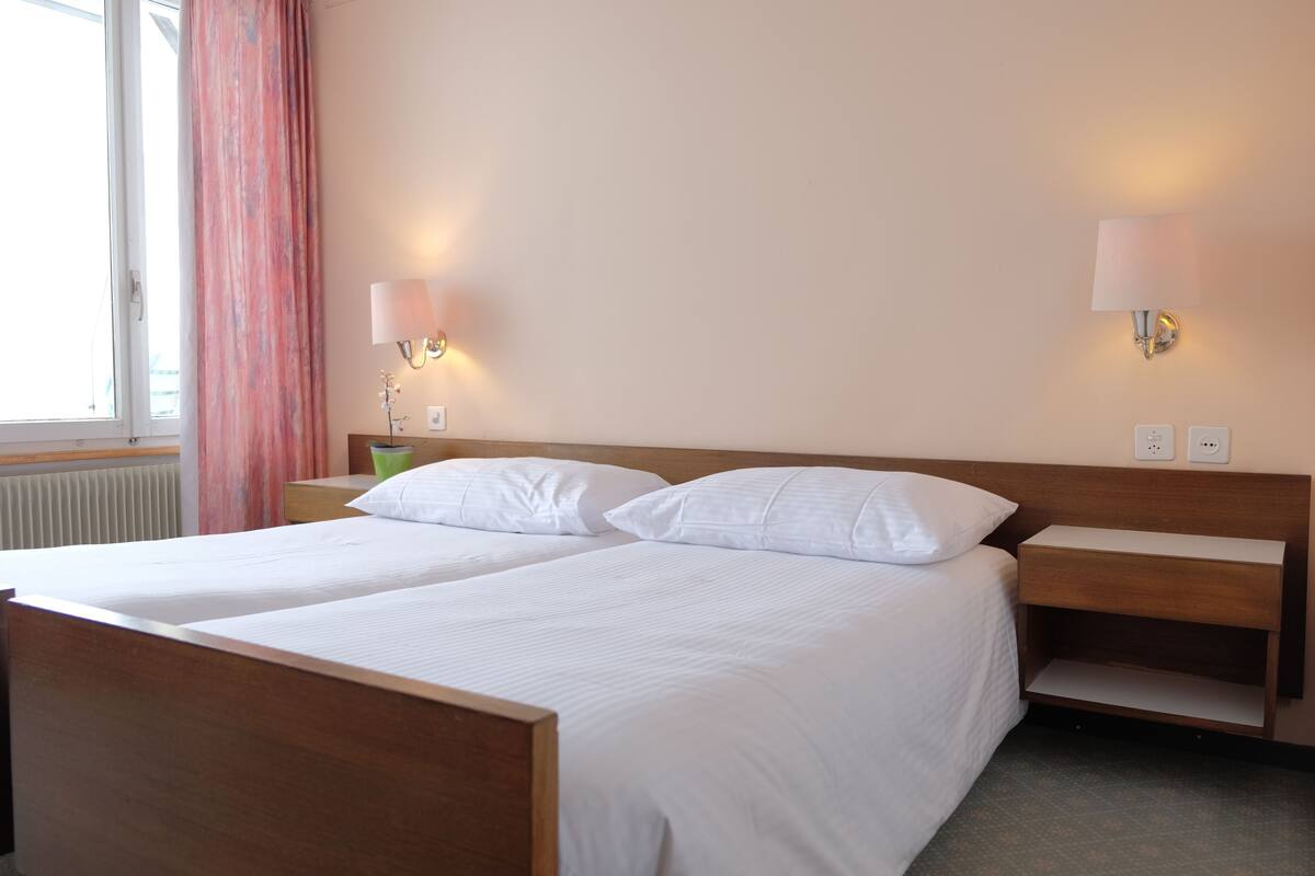 A double bed with white linens, two bedside tables, and wall-mounted lamps.