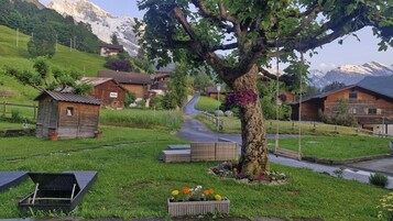 Un pueblo rural con casas de madera tradicionales, un camino sinuoso y un gran árbol con flores colgantes.