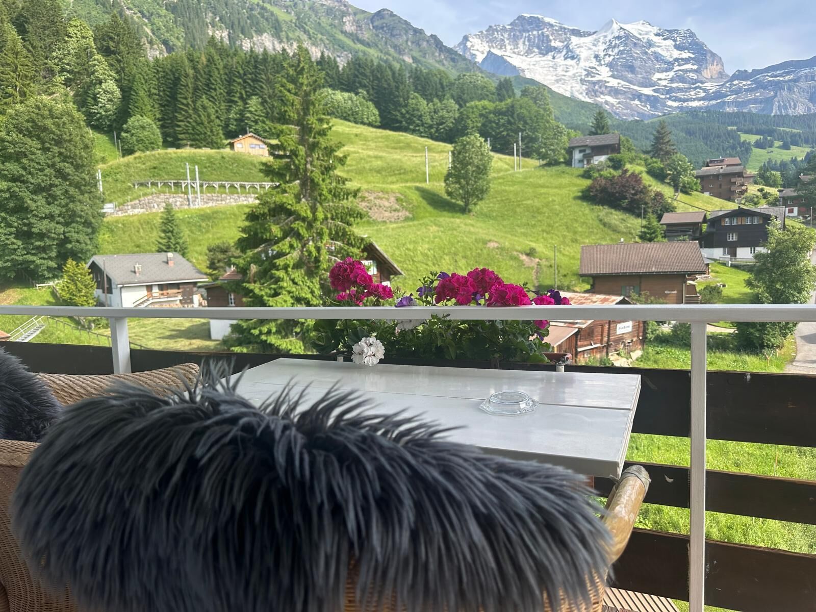 A balcony with a view of a mountainous landscape, a table with a glass, and a wicker chair.