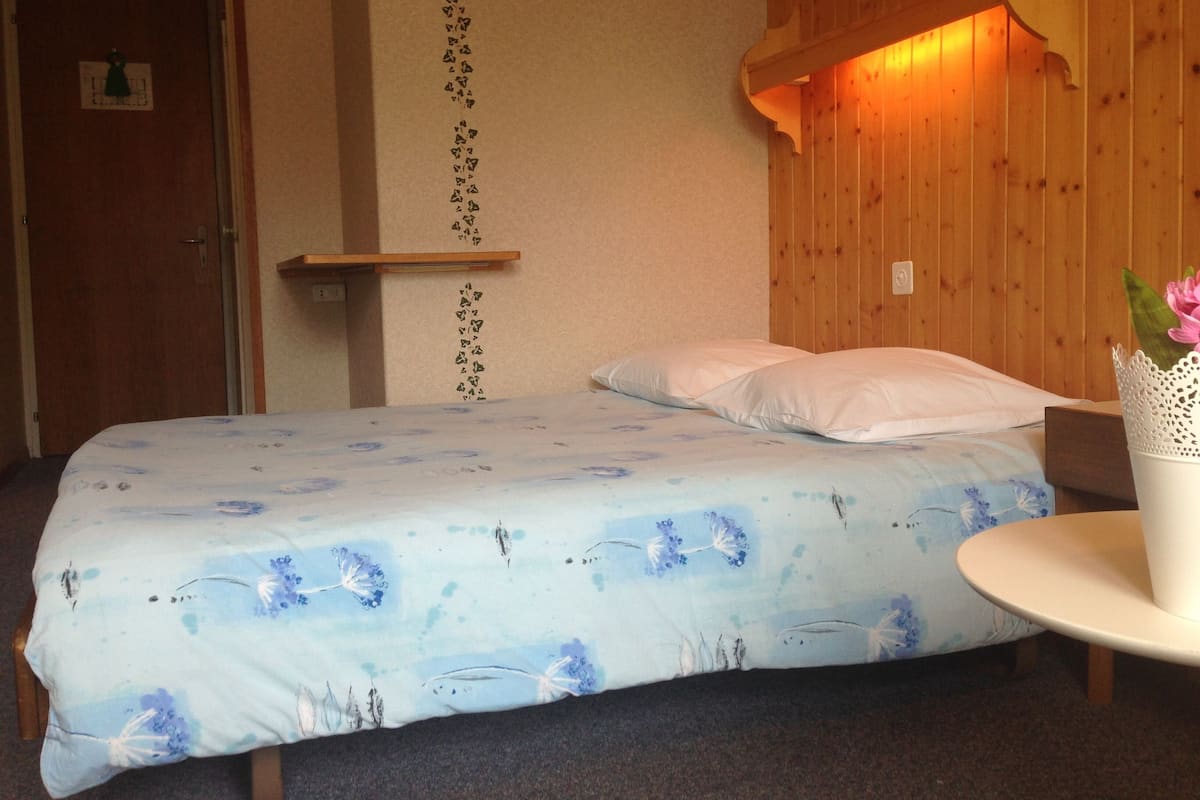 A bedroom with a bed, pillows, a bedside table, and a wall-mounted shelf.