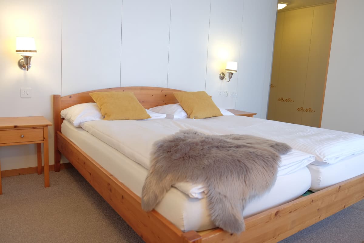 A wooden bed with white bedding and two yellow pillows, a nightstand, and two wall-mounted lamps.
