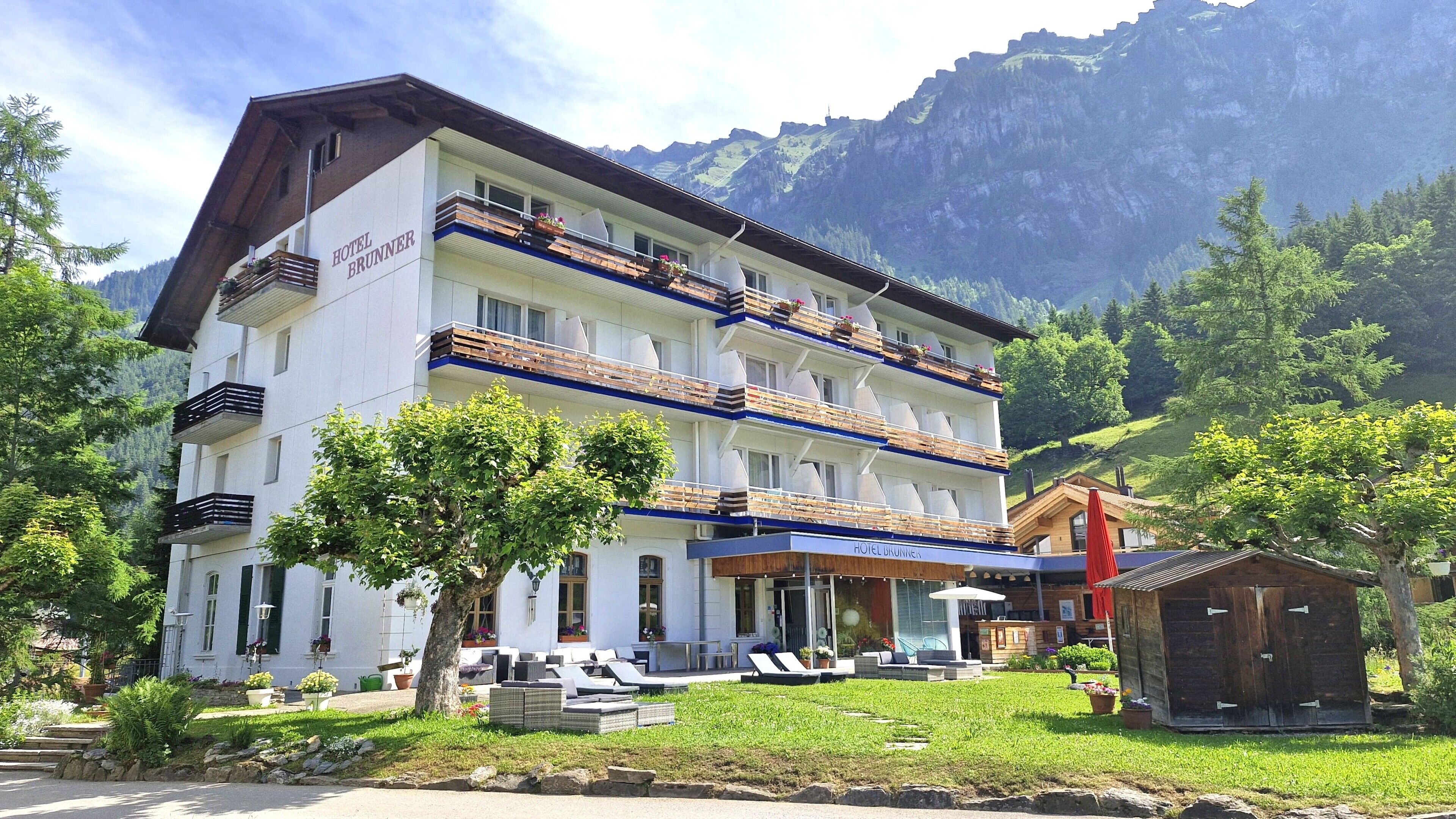 Un hotel de varios pisos con balcones, una zona de piscina y montañas al fondo.