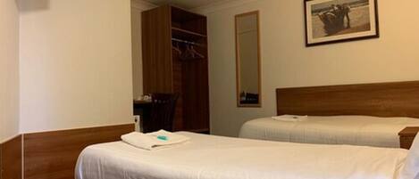 A hotel room with two beds, a wooden wardrobe, a television, a mirror, and a framed picture on the wall.