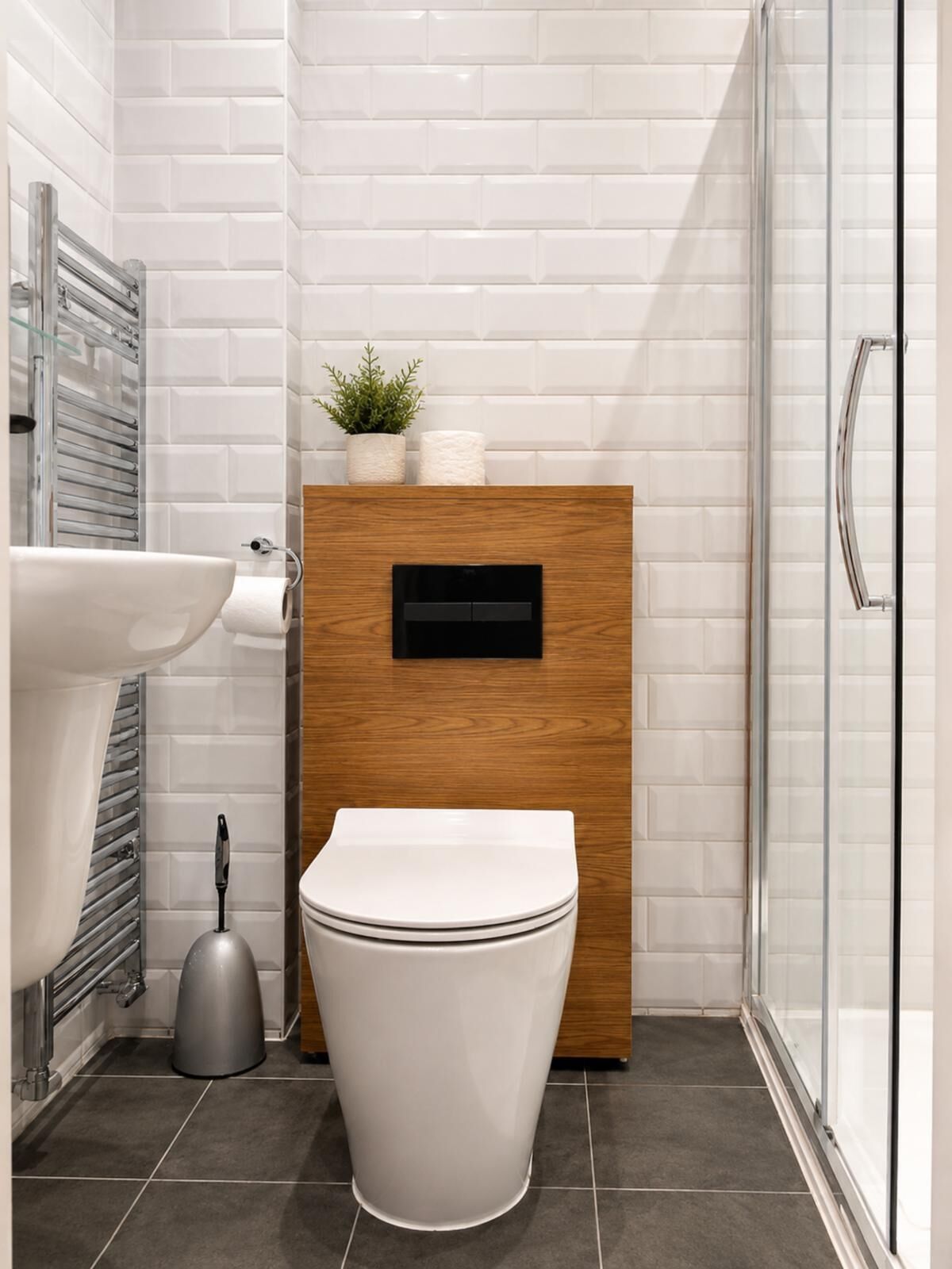 A modern bathroom with a white toilet, a wooden cabinet, a glass shower enclosure, and a sink.