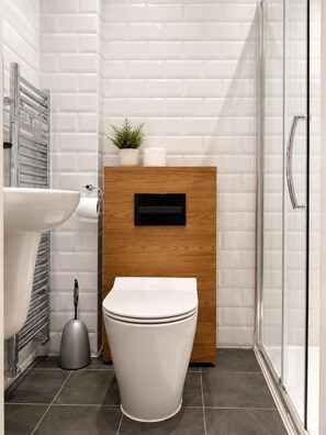 A modern bathroom with a white toilet, a wooden cabinet, a glass shower enclosure, and a sink. - Twickenham Guest House (Twickenham)