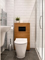 Un baño moderno con inodoro blanco, mueble de madera, cabina de ducha de vidrio y lavamanos.