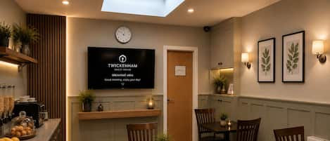 A breakfast area with a clock, a TV displaying 'TWICKENHAM GUEST HOUSE BREAKFAST AREA,' and a 'STAFF ONLY' sign.