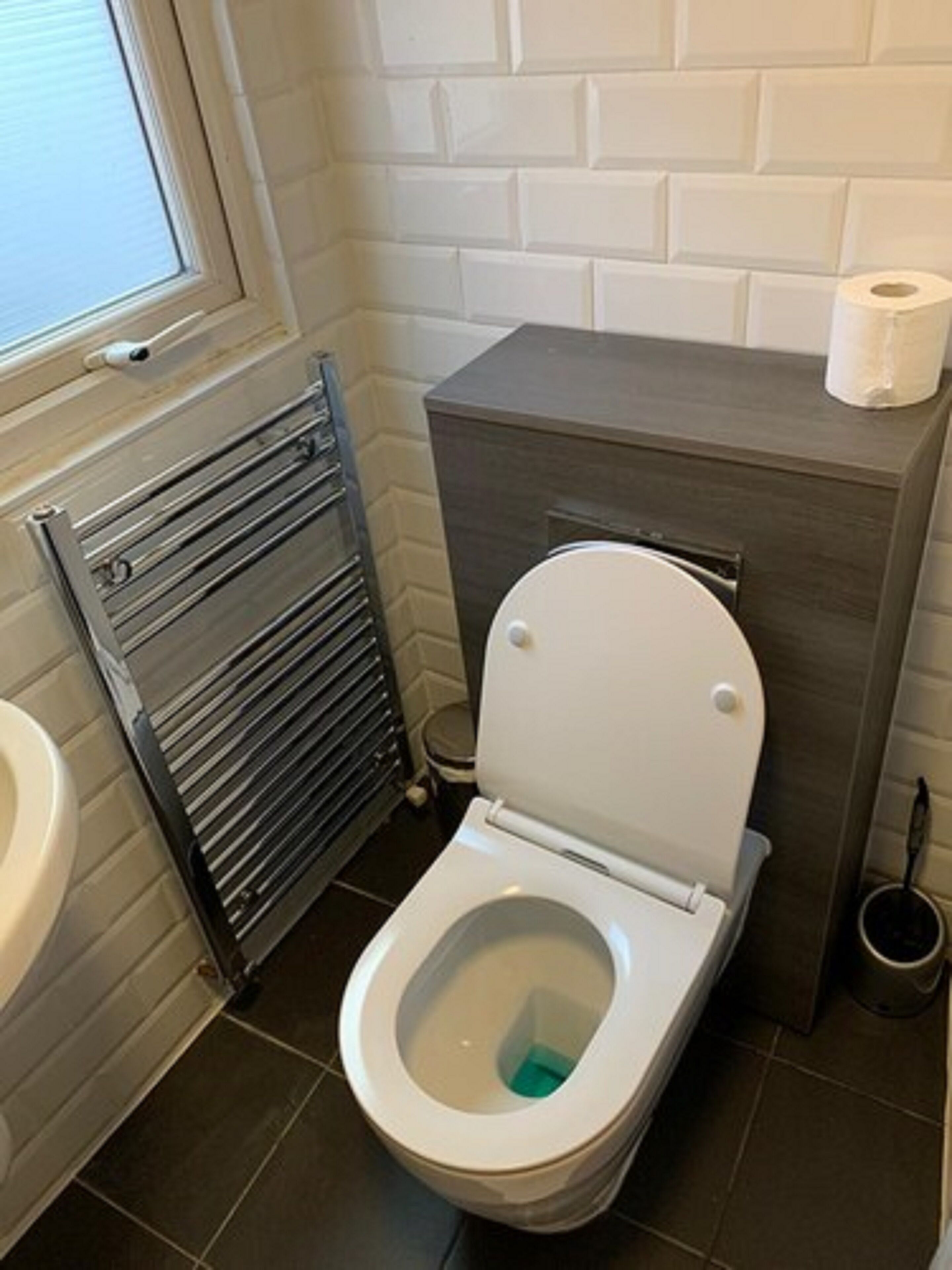A small bathroom with a toilet, a towel rack, and a window.