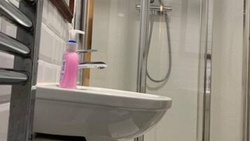 A modern bathroom with a glass-enclosed shower, a white sink, and a bottle of soap.