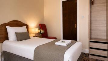 Una habitación de hotel con cama, mesita de noche, lámpara, silla y armario.