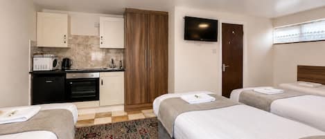 A hotel room with a kitchenette, two beds, a TV, and a patterned rug.