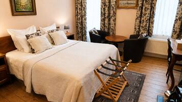 Une chambre d’hôtel avec un lit, un plancher en bois, un lustre, une table à manger et des rideaux.