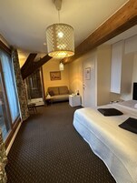A hotel room with a large bed, a sofa, a small table, a shower area, and a staircase.