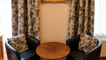 A room with a round wooden table, two black leather chairs, and patterned curtains.