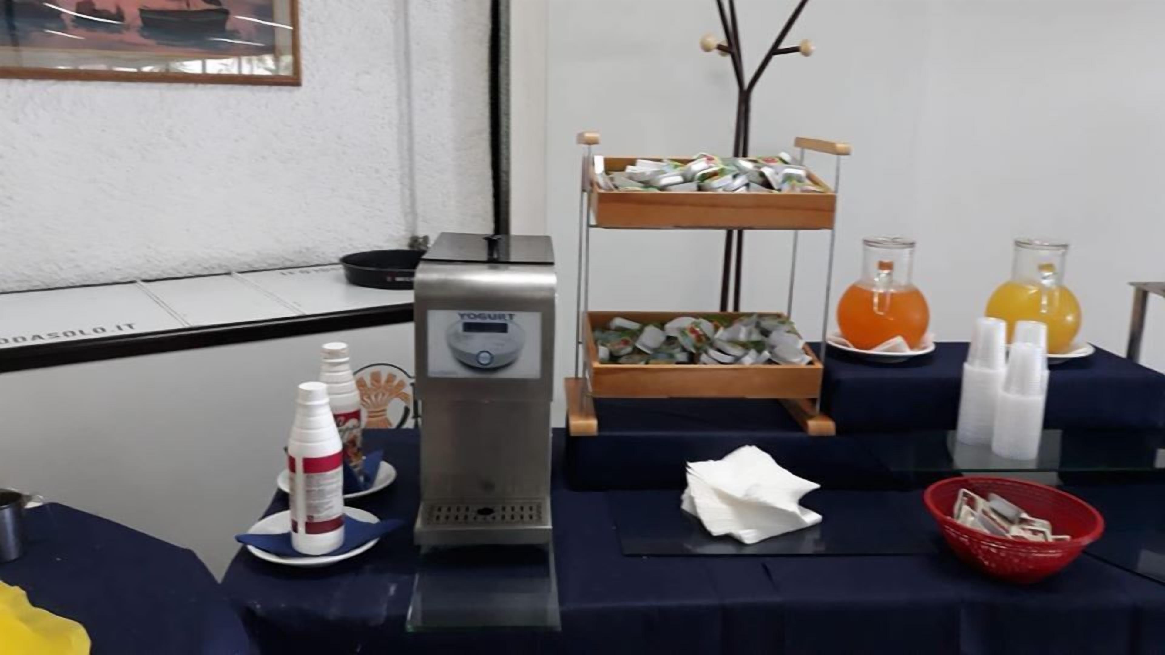 Un buffet con erogatore per yogurt, due ripiani pieni di contenitori per alimenti e due caraffe di succo d'arancia.