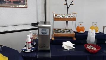 Un buffet con erogatore per yogurt, due ripiani pieni di contenitori per alimenti e due caraffe di succo d'arancia.