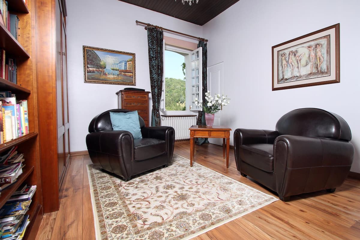 Una sala de estar con dos sofás de cuero, una estantería de madera, un tapete estampado, una mesa de centro de madera y una ventana con cortinas.