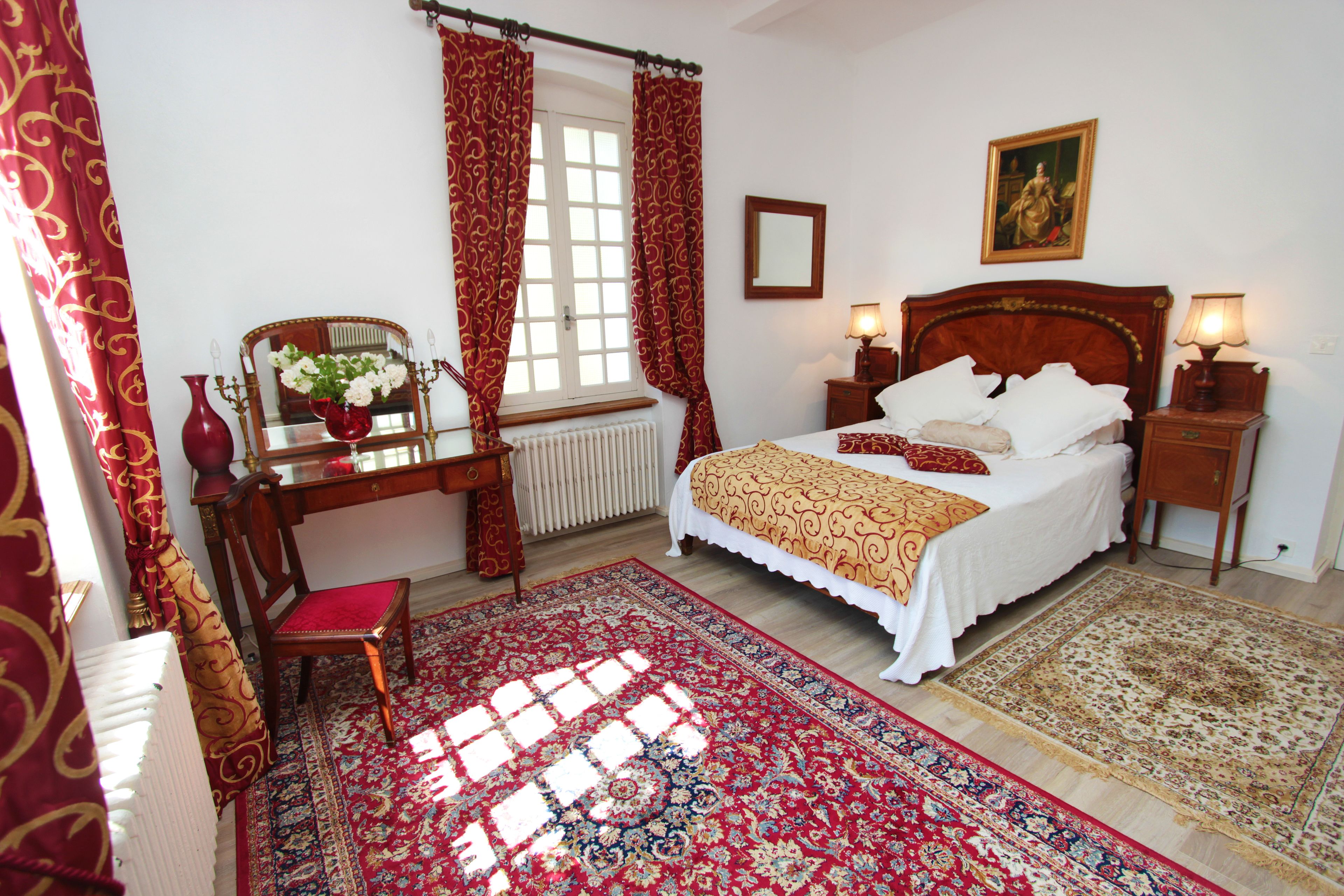 A bedroom with a bed, a desk with a chair, a window with curtains, a radiator, and a painting on the wall.