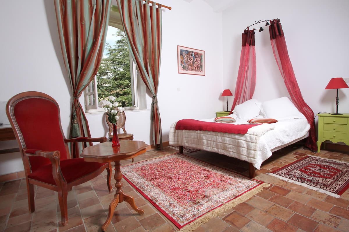 Un dormitorio con cama, una silla, una mesa y una ventana con cortinas.