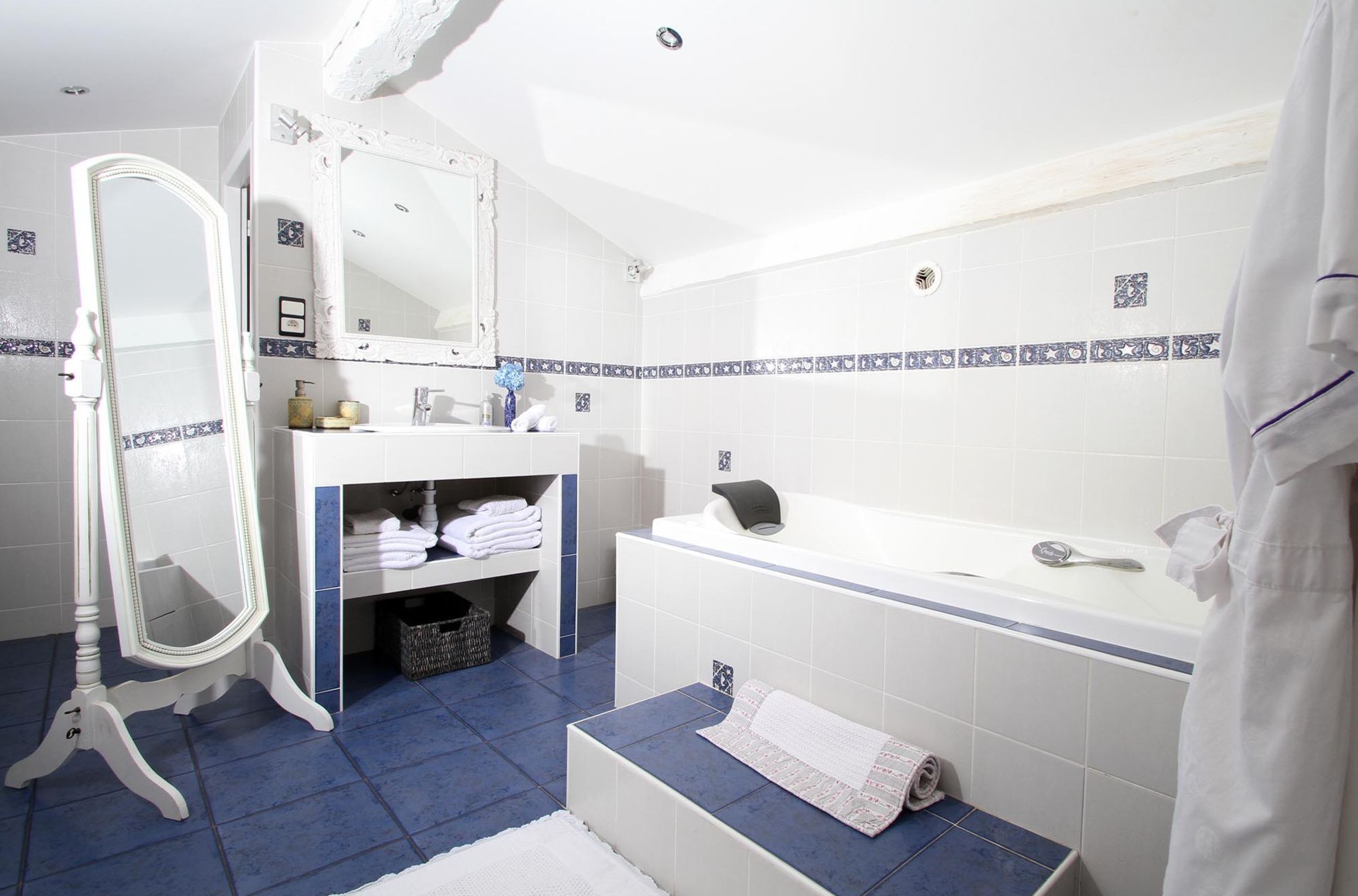 A bathroom with a white vanity, a large mirror, a bathtub, and blue-tiled flooring.