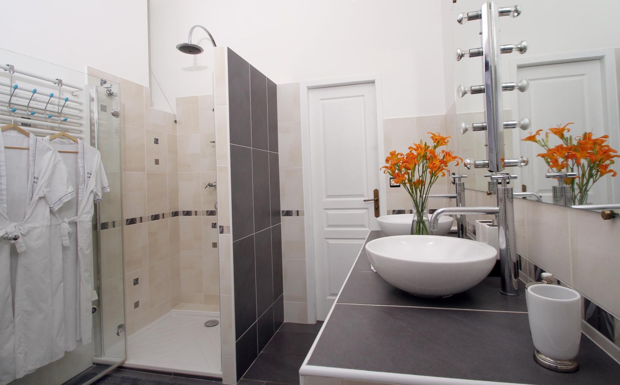 A modern bathroom with a walk-in shower, a large sink, and a mirror with a vase of flowers.