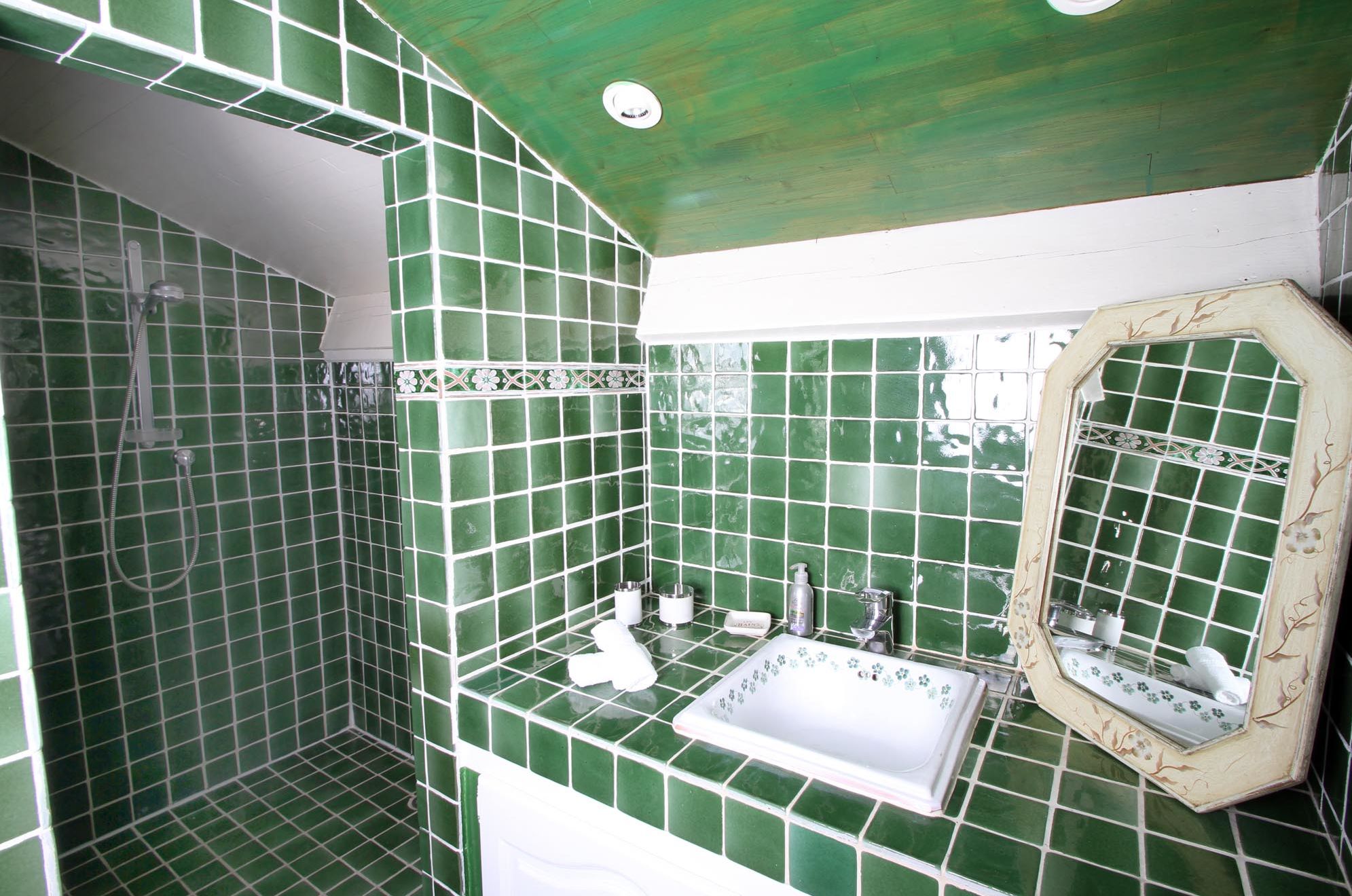 A bathroom with green tiles, a sink, a mirror, and a shower.